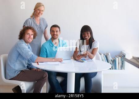 Were the team you need. four coworkers gathered around a laptop in the office. Stock Photo