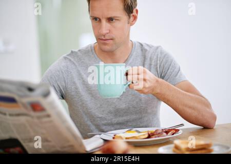 Lets see whats happening in the world...a handsome man reading the paper while having breakfast. Stock Photo