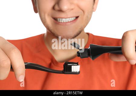 Man applying charcoal toothpaste onto toothbrush on white background, closeup Stock Photo