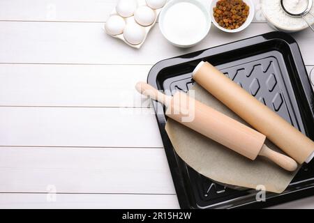 Baking pan with parchment paper, different ingredients and kitchen tools on white wooden table, flat lay. Space for text Stock Photo