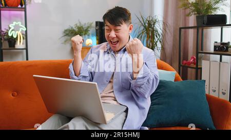 Oh my God Wow. Surprised asian man using laptop computer, receive good news message, shocked by sudden victory, celebrate lottery jackpot win, purchases online shopping at home. Lifestyle technologies Stock Photo