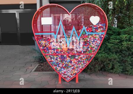 Heart shaped red recycling container for plastic caps outdoors Stock Photo