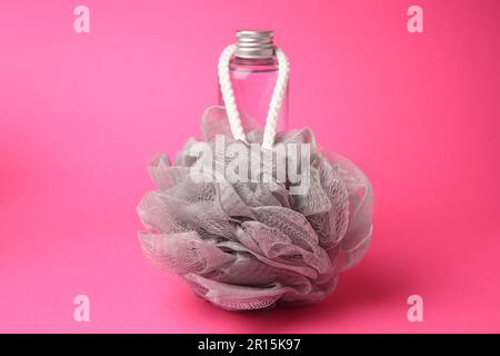 Grey shower puff and bottle of cosmetic product on pink background Stock Photo