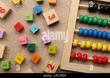 Wooden cubes with numbers and multiplications near abacus on fiberboard, flat lay Stock Photo