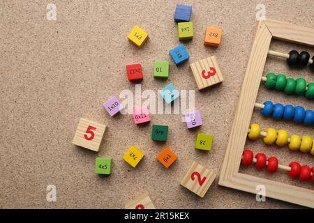 Wooden cubes with numbers and multiplications near abacus on fiberboard, flat lay. Space for text Stock Photo