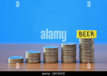 A row of a growing stack of coins illustrating the increasing cost of Beer due to the rising cost of living, on a blue background with copy space Stock Photo