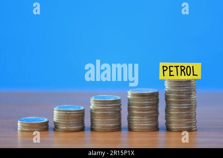 A row of a growing stack of coins illustrating the increasing cost of Petrol due to the rising cost of living, on a blue background with copy space Stock Photo