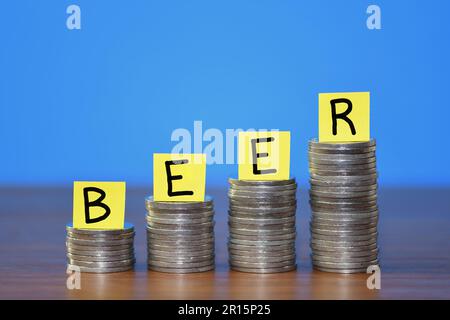 A row of a growing stack of coins illustrating the increasing cost of Beer due to the rising cost of living, on a blue background with copy space Stock Photo