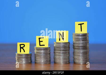 A row of a growing stack of coins illustrating the increasing cost of household Rent due to the rising cost of living, on a blue background Stock Photo