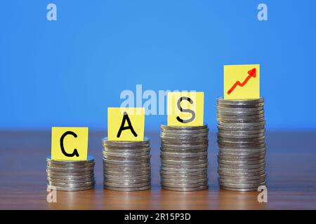 A row of a growing stack of coins illustrating the increasing cost of Gas due to the rising cost of living, on a blue background with copy space Stock Photo