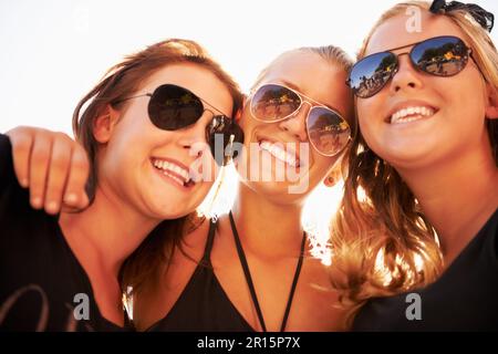 Soaking up the sun. Three friends hugging and smiling against a bright sky. Stock Photo