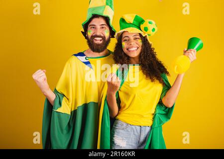 couple of brazil soccer supporters, dressed in the colors of the nation, black woman, caucasian man. using flag and accessories Stock Photo