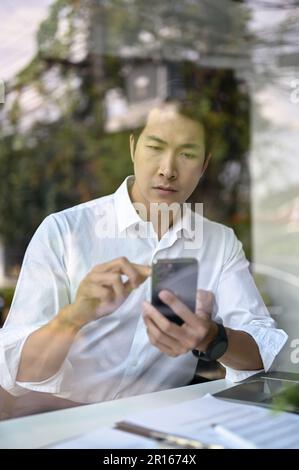 Portrait of a focused and professional millennial Asian businessman or male CEO checking his messages on his smartphone while working in his office. Stock Photo