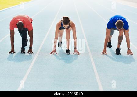 Committed from the start. Full length shot of three young athletes in the set position out on the running track. Stock Photo
