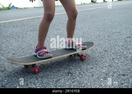 Cute little girl learns how to skateboard at outdoor street, focus on legs standing on board. Healthy sports and outdoor activities for school childre Stock Photo