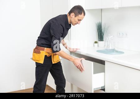 Young Handyman In Overall Installing Drawer In Kitchen Stock Photo