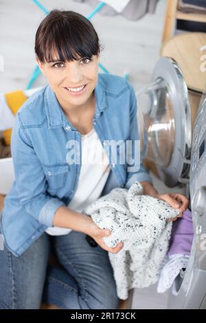 woman crouching with cleaned clothes near the electronic washer Stock Photo