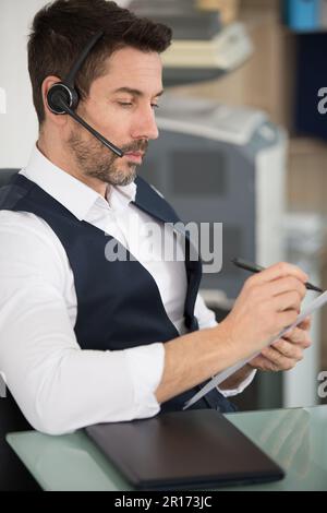 businessman wearing headset with microphone taking notes Stock Photo