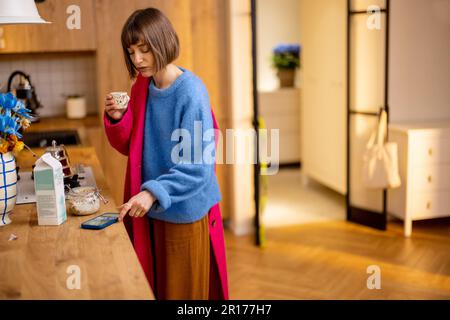 Woman rushes out of home putting on a coat and finishing her coffee Stock Photo