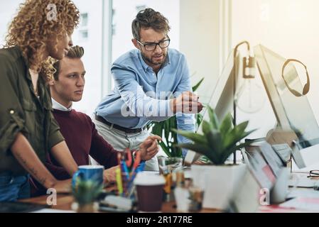 Getting ready to launch an online campaign. a group of colleagues using a computer together in a modern office. Stock Photo