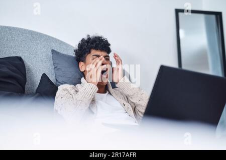 Sports bar closed Stream the game instead. a young man looking shocked while using a laptop on his bed at home. Stock Photo