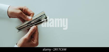 high angle view of a man wearing a white long-sleeve shirt counting some dollar notes at a white table, in a panoramic format to use as web banner Stock Photo
