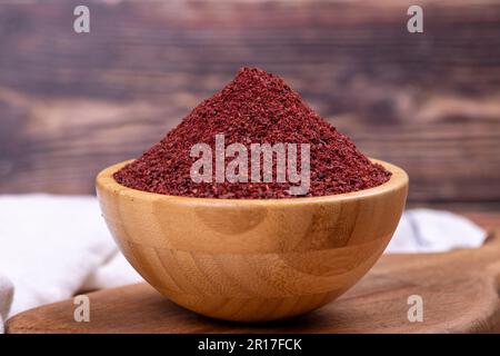 Sumac on wooden background. Dried ground red Sumac powder spices in wooden bowl. Close up Stock Photo