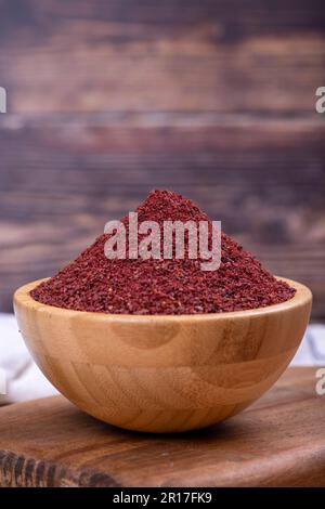 Sumac on wooden background. Dried ground red Sumac powder spices in wooden bowl. Close up Stock Photo