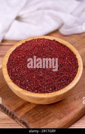 Sumac on wooden background. Dried ground red Sumac powder spices in wooden bowl. Close up Stock Photo