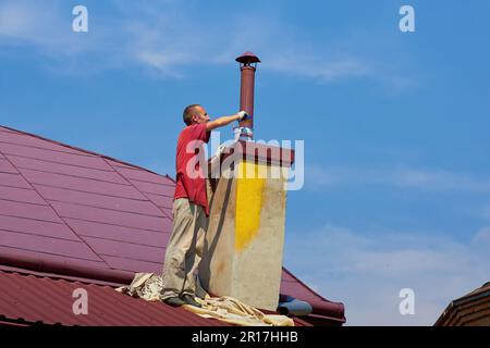 man works on the roof painting the chimney Stock Photo