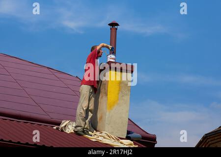 in dirty clothes a man paints a chimney on the roof Stock Photo