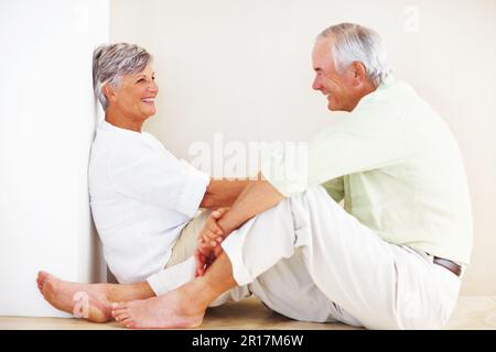 Mature couple spending time at home. Smiling mature couple spending time at home while sitting on ground. Stock Photo