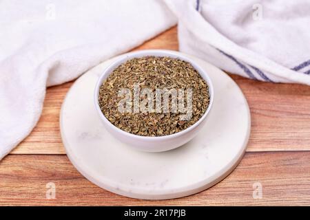 Dried crushed basil on wooden background. Dried ground basil powder spices in ceramic bowl. Spice concept Stock Photo