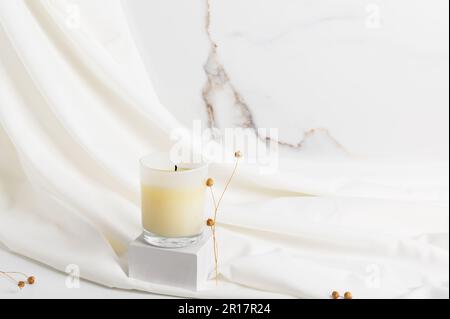 Natural wax candle on a white podium and fabric background. Stock Photo