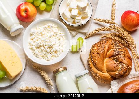 Jewish holiday Shavuot concept with dairy products, cheese, bread, milk bottles, wheat and grapes close up, flat lay. Stock Photo