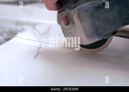 A construction worker saws ceramic tiles using an angle grinder Stock Photo
