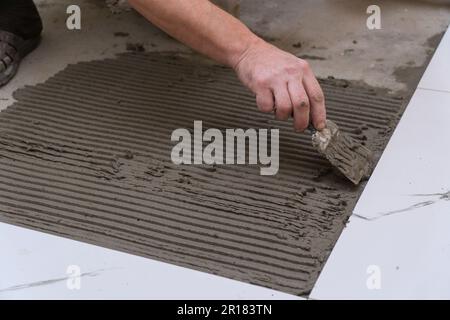 A construction worker applies cement for laying floor ceramic tiles with a spatula. Selective focus Stock Photo