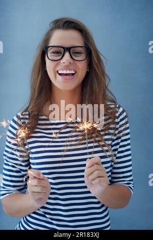 Have a super sparkly day. Studio shot of a beautiful young woman holding sparklers against a blue background. Stock Photo