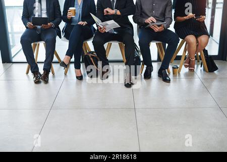 Its getting closer to the time. a group of unrecognizable businesspeople sitting in line for an interview in a modern office. Stock Photo