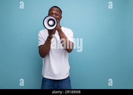 casual 30s african man with short hair in white t-shirt speaks into loudspeaker interesting news Stock Photo
