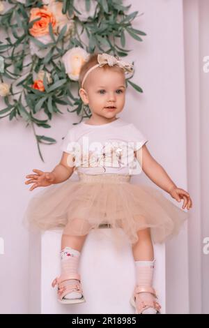 Baby girl elegant dress. A one-year-old girl in a puffy skirt and a white  T-shirt poses against the backdrop of a bright room with a yellow tulip in  Stock Photo - Alamy