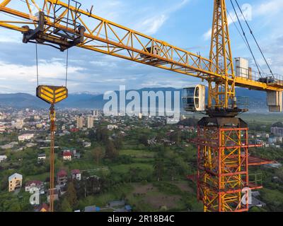 Close-up view from a drone of a construction crane cabin against the backdrop of beautiful mountains and sky. Construction concept Stock Photo