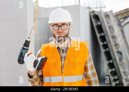 Repairman worker in uniform and helmet holding cordless screwdriver, standing on his workplace. Stock Photo