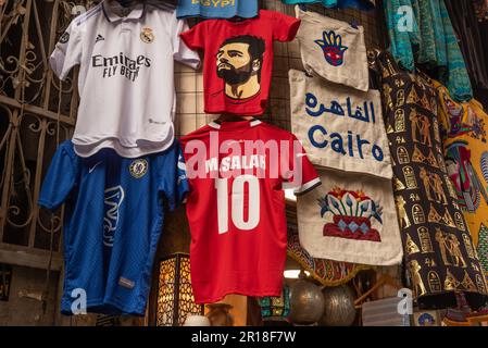 Egyptian, Mo Salah football shirts seen being sold as tourist souvenirs in the famous Khan El Khalili Bazaar in Islamic Cairo, Egypt. Cairo, Egypt's sprawling capital located on the banks of the River Nile, known in Arabic as Al Qahirah, meaning 'The Victorious' is an ever-expanding megacity with a population of over 20 million people. Stock Photo