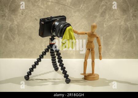 A photo of a wooden Mannequin  cleaning the lens of an small modern digital camera Stock Photo