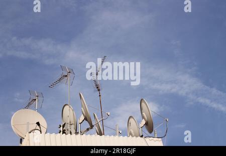 Center for satellite dishes and digital terrestrial television antennas on a roof in a large city. Copy space with blue sky with aircraft contrails Stock Photo