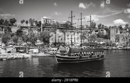 A tourist boat sails through the ancient harbour in Kaleici, the charming old town in Antalya, Turkey, on a sunny day. The boat is just one of many th Stock Photo