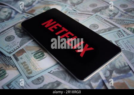 Netflix logo displayed on smartphone on top of pile of money. Stock Photo