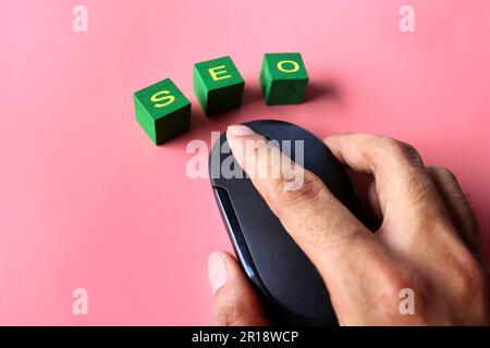 Hand click computer mouse with text SEO on pink background. Search engine optimization concept. Stock Photo