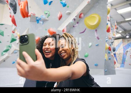 Two Smiling Female Friends Posing For Selfie By Climbing Wall At Indoor Activity Centre Stock Photo